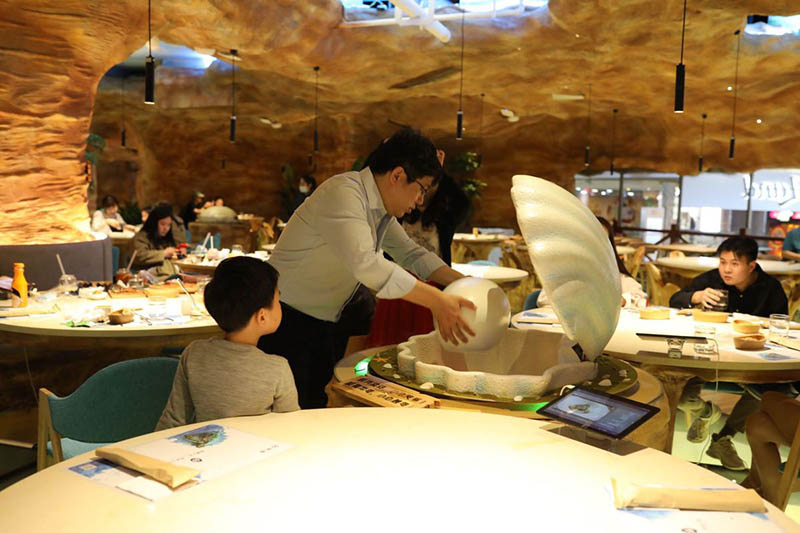 Un camarero sirve comida dentro de un recipiente con forma de perla para los comensales en Caretta Land, un restaurante temático sobre robots tortuga en Shanghai. [Foto proporcionada a chinadaily.com.cn]